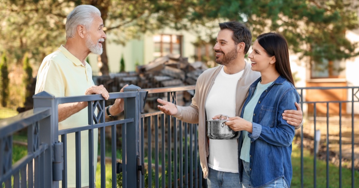 Young couple bringing food to their elderly neighbor over a garden fence