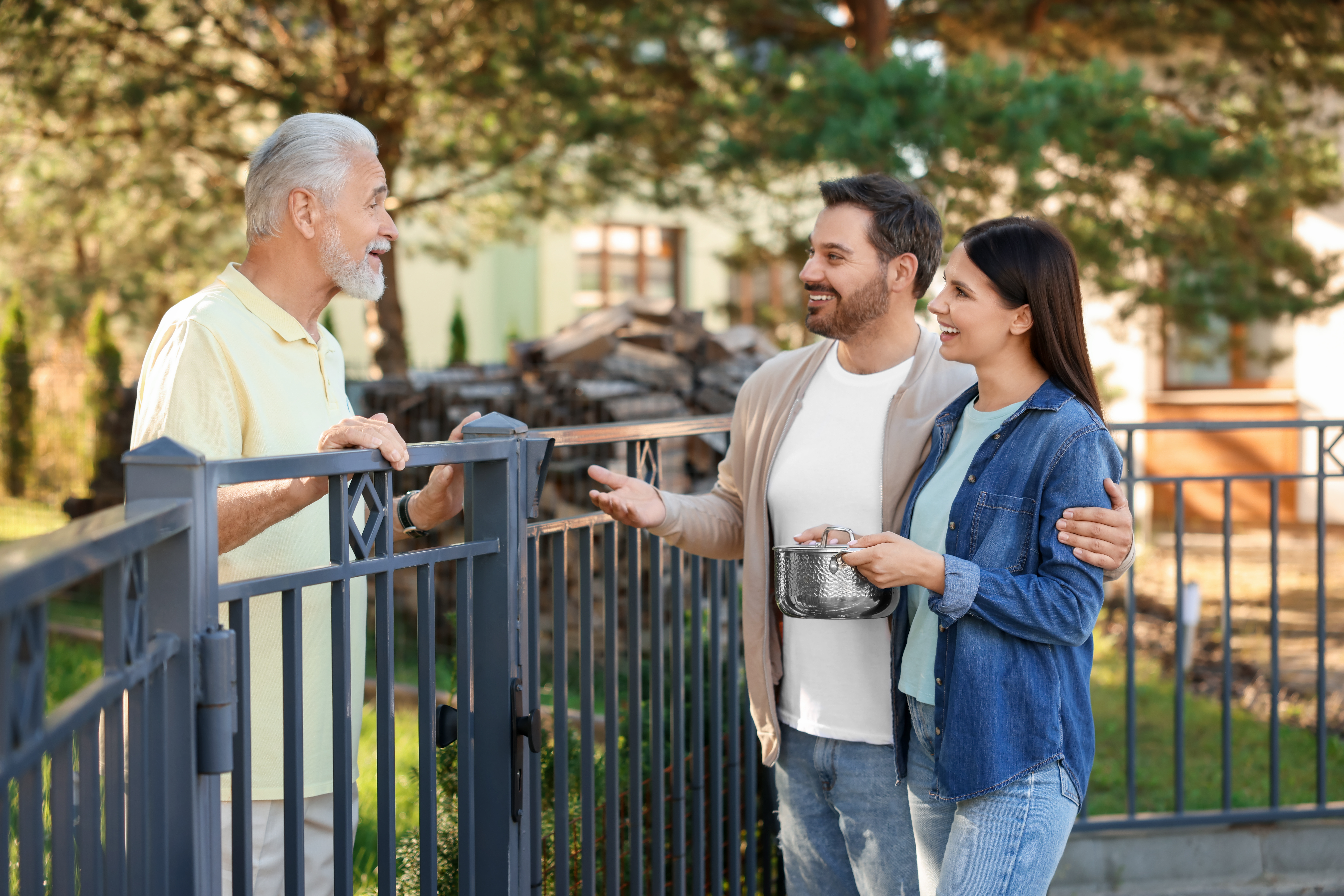 Young couple bringing food to their elderly neighbor over a garden fence